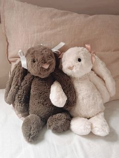 two stuffed animals sitting on top of a bed next to each other, one brown and one white