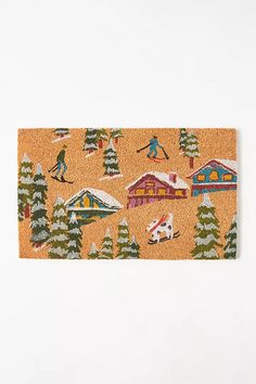 an orange door mat with skiers and houses on it, in front of a white wall