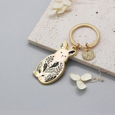 a gold keychain with a bird on it and a small white butterfly next to it