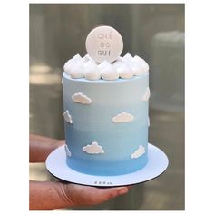 a hand holding a blue and white cake with clouds on it