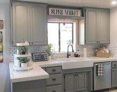 a kitchen with gray cabinets and white counter tops, an open window above the sink