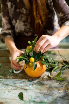 a woman is arranging an orange with leaves and fruit on the top, as if it were for decorating