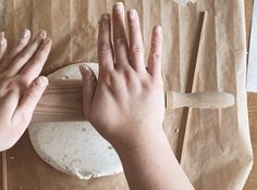 two hands on a piece of paper with dough in front of them and one hand reaching for something