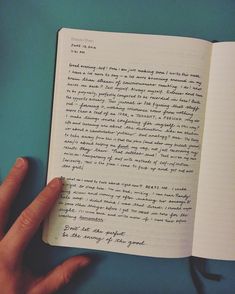 a hand holding an open book with writing on it