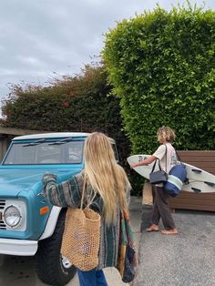 two women carrying surfboards walking towards a blue truck