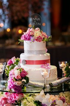 a wedding cake with pink and white flowers on it sitting on a table in front of candles