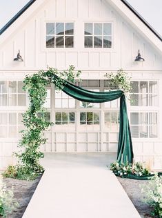 an outdoor wedding venue with green drapes and white flowers on the aisle, surrounded by greenery