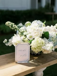 a bouquet of white flowers sitting on top of a wooden table next to a sign