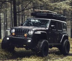 a black jeep parked in the woods with its lights on