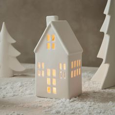 a small white house sitting on top of a snow covered ground next to two trees