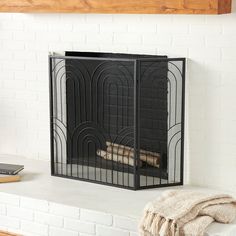 a fireplace screen sitting on top of a mantle next to a book and a blanket