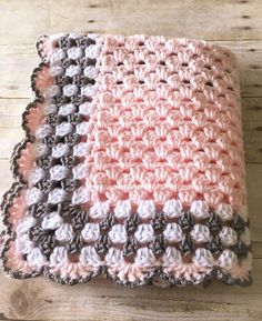 a crocheted blanket is laying on a wooden floor with white and pink colors