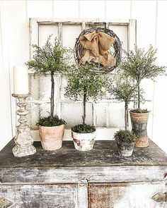 an old dresser with potted plants and a wreath on the front window sill