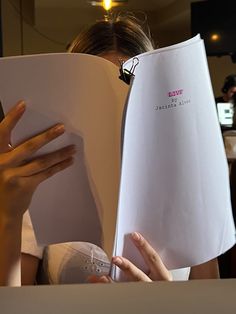 a woman is reading a book with her hands on the page and holding it open