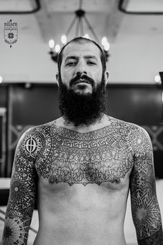 a man with tattoos on his chest standing in front of a mirror and looking at the camera