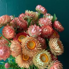 a vase filled with pink and yellow flowers on top of a wooden table next to a green wall