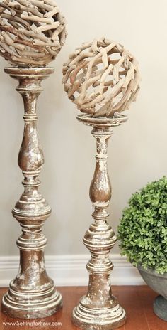 two metal candlesticks sitting on top of a wooden table next to a potted plant