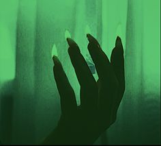 a person's hand with green nail polish on their nails, in front of a window