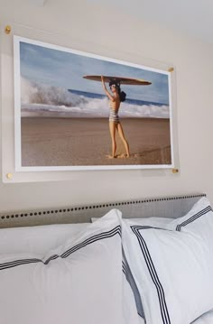 a woman holding a surfboard over her head on a bed with white sheets and pillows