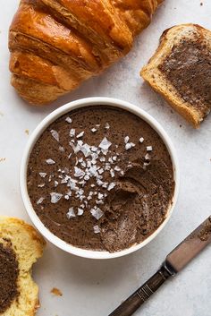 there is a bowl of chocolate pudding next to some croissants and bread