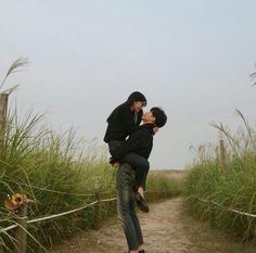 a man holding a woman on his back while walking down a path through tall grass