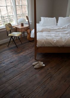 a bed sitting in a bedroom next to a window with white sheets and pillows on top of it