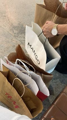 a person sitting on the ground with several bags in front of them and one holding a watch