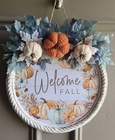 a welcome fall sign hanging on the front door with pumpkins and leaves around it