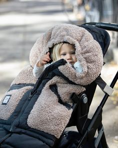 a small child in a stroller with a hood over it's head and one hand on the handle