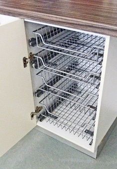 an open cabinet with wire baskets on the bottom and drawers below it, in a kitchen