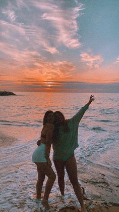 two women are standing on the beach at sunset