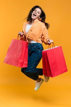 a woman jumping in the air with shopping bags on her back and smiling at the camera