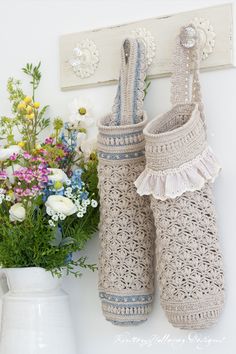 two crocheted boots are hanging on the wall next to flowers and a vase