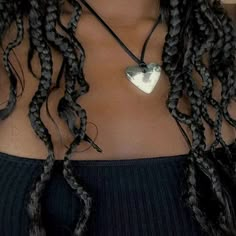 a close up of a woman with braids and a heart pendant on her necklace