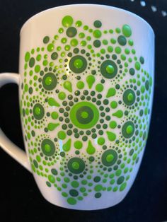 a green and white coffee cup with circles painted on the side, sitting on a black surface