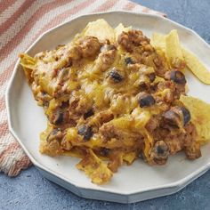 a white plate topped with nachos covered in meat and cheese next to tortilla chips