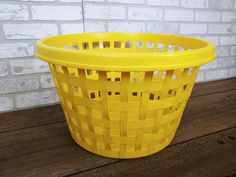 a yellow plastic basket sitting on top of a wooden table next to a brick wall