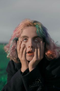 a woman with pink hair holding her hands to her face and looking at the camera