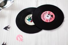 two black vinyl records sitting on top of a white table cloth next to spoons