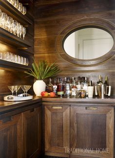 a bar with lots of liquor bottles and glasses on it's counter top, next to a round mirror