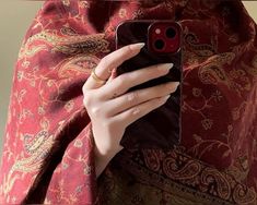 a woman is holding her cell phone while wearing a red shawl and gold ring