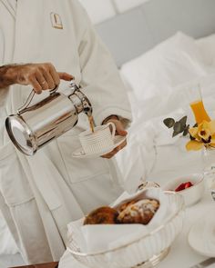 a man in white robe pouring coffee into a cup on top of a tray with pastries