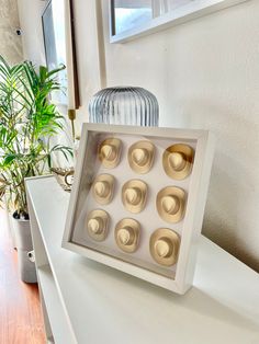 a white table topped with an open box filled with gold cupcakes next to a potted plant