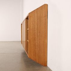 a wooden cabinet sitting in the middle of a room next to a white wall and floor