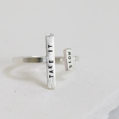 One of our favorite gift-able rings, the Double Adjustable Ring is an eye-catching way to inspire & encourage. An adjustable, asymmetric ring with a tiny phrase of inspiration. Letters are individually stamped by hand, making each ring one of a kind. The message is centered on each bar in our signature teeny-tiny uppercase block font. For an unconventional look, try stacking with our diamond dusted adjustable rings. details+ longer bar measures 5/8" wide x 2 mm tall+ shorter bar measures 1/4" wi Modern Adjustable Stackable Promise Rings, Modern Adjustable Stackable Rings As A Gift, Modern Adjustable Stackable Rings For Gifts, Modern Adjustable Midi Rings For Promise, Adjustable Hand Stamped Midi Rings, Adjustable Open Ring With Meaningful Style, Adjustable Inspirational Sterling Silver Rings, Inspirational Adjustable Hand Stamped Rings, Inspirational Adjustable Sterling Silver Rings