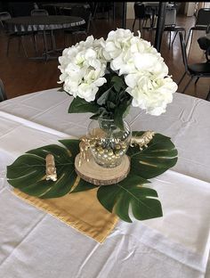 white flowers in a vase on top of a table with gold napkins and green leaves