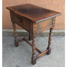 an old wooden table with turned legs on concrete ground next to brick wall and door