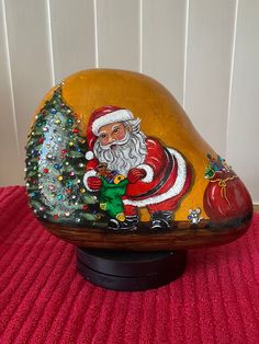 a rock with a santa clause painted on it and a christmas tree in the corner