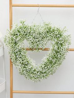 a heart shaped wreath hanging from a wooden frame next to a white wall and chair