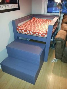 a blue bed with a red and white pillow on it next to a brown couch